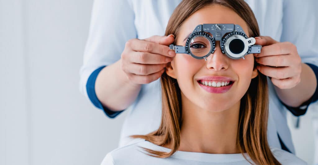 Femme souriante lors d'un examen de la vue, un optométriste ajuste un phoroptère. Contrôle de la vision et santé oculaire.