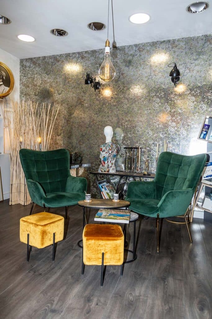 Salon cosy : Fauteuils velours et déco murale design Coin salon cosy avec deux fauteuils vert émeraude velours, poufs moutarde, table basse ronde, et papier peint floral sur fond sombre.